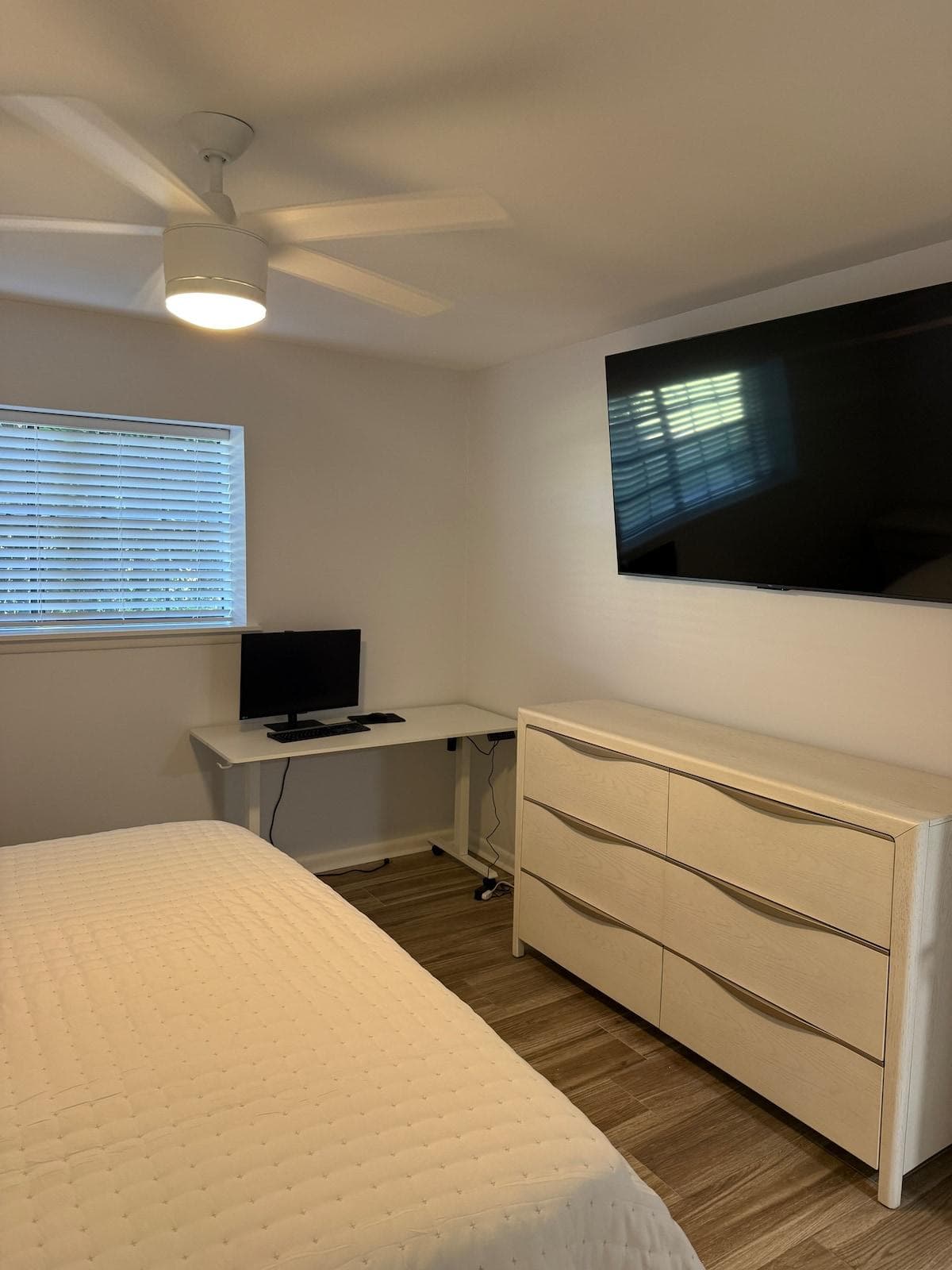 Master bedroom with king size bed, television, and work area with adjustable desk, monitor, keyboard and mouse